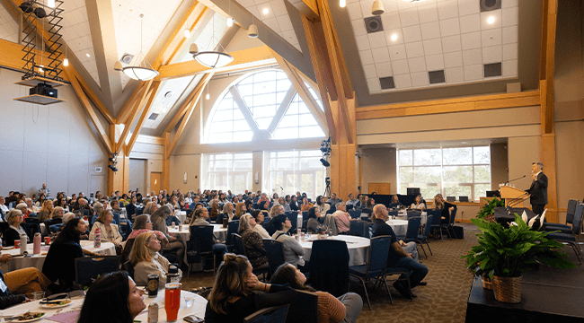 a large group of people listening to a speaker at a conference