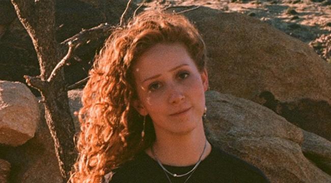 a person sitting outdoors with rocks and a dead tree branch in the background.