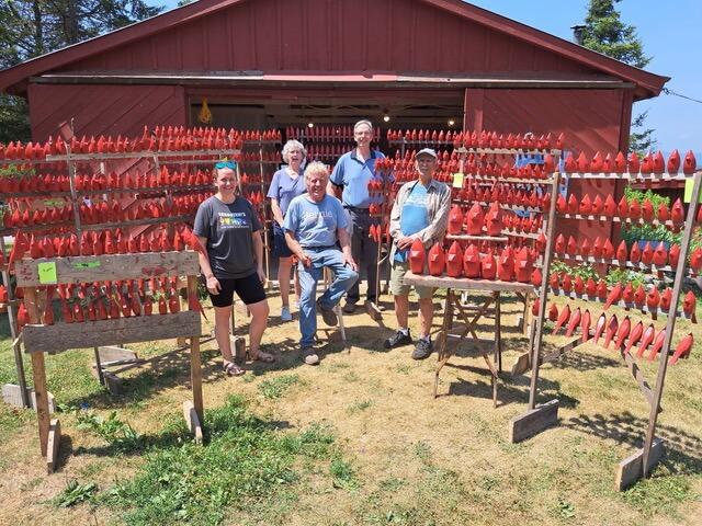 5 people standing in a clearing surrounded by racks of red carved wooden cardinals