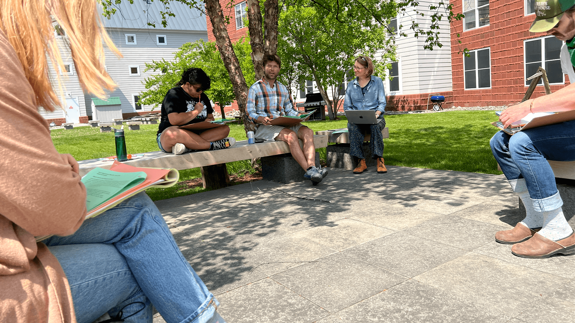 UVM faculty seated outside in a shaded courtyard, working on assignments.