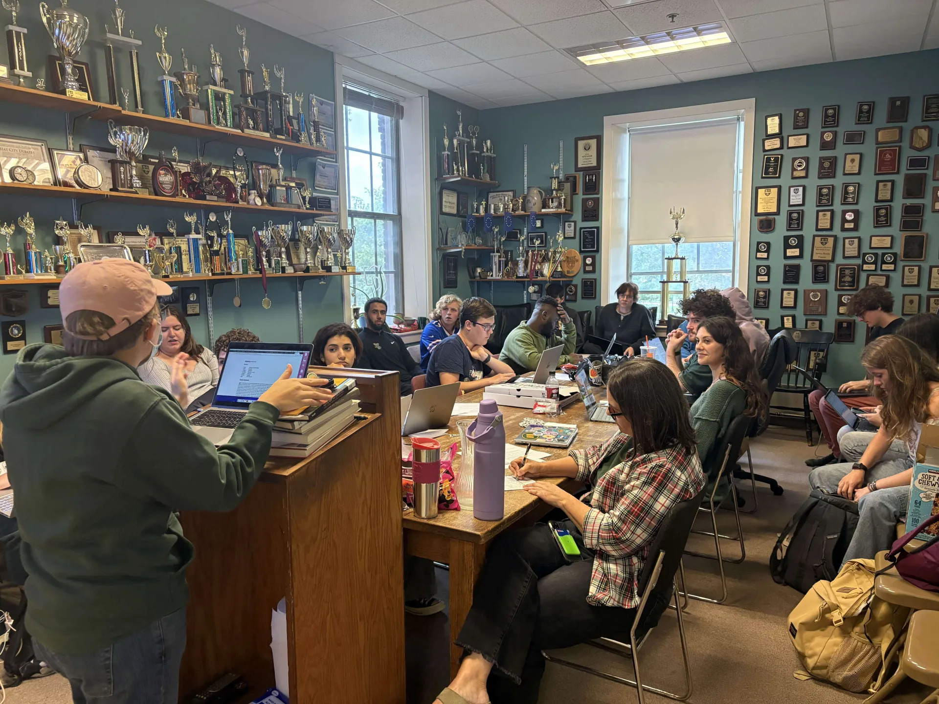 Students gathered in a meeting room with trophies and plaques on the walls.