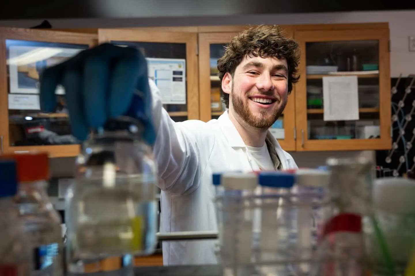 Student in lab coat reaching for glass containers