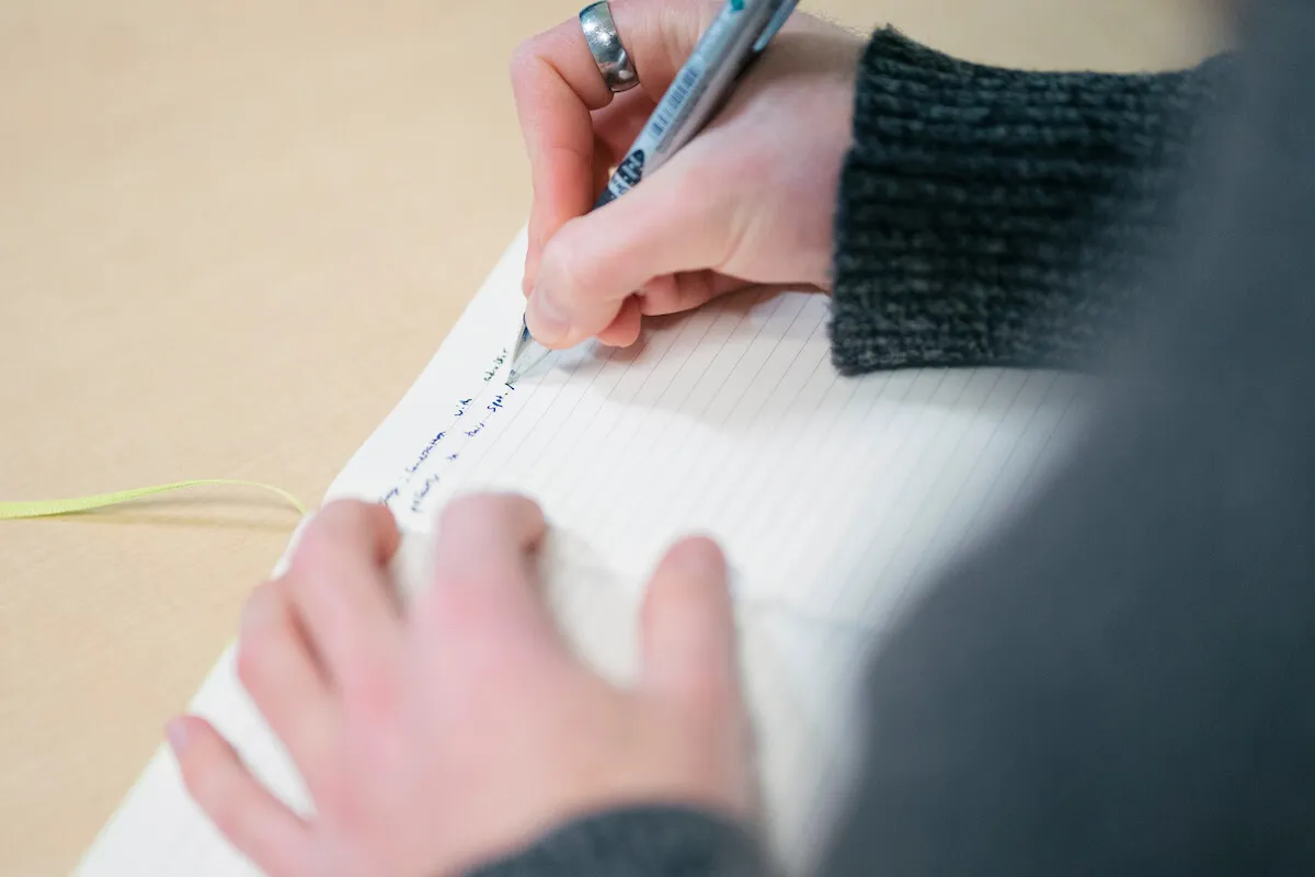 Close-up of a person writing in a lined notebook with a pen.