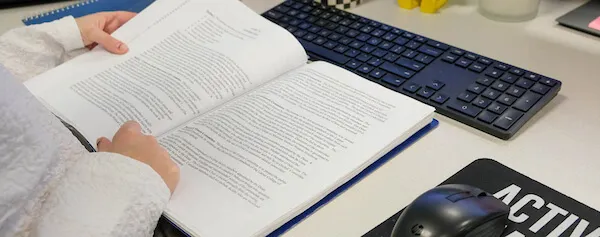 someone reading a book that is laying on top of a keyboard