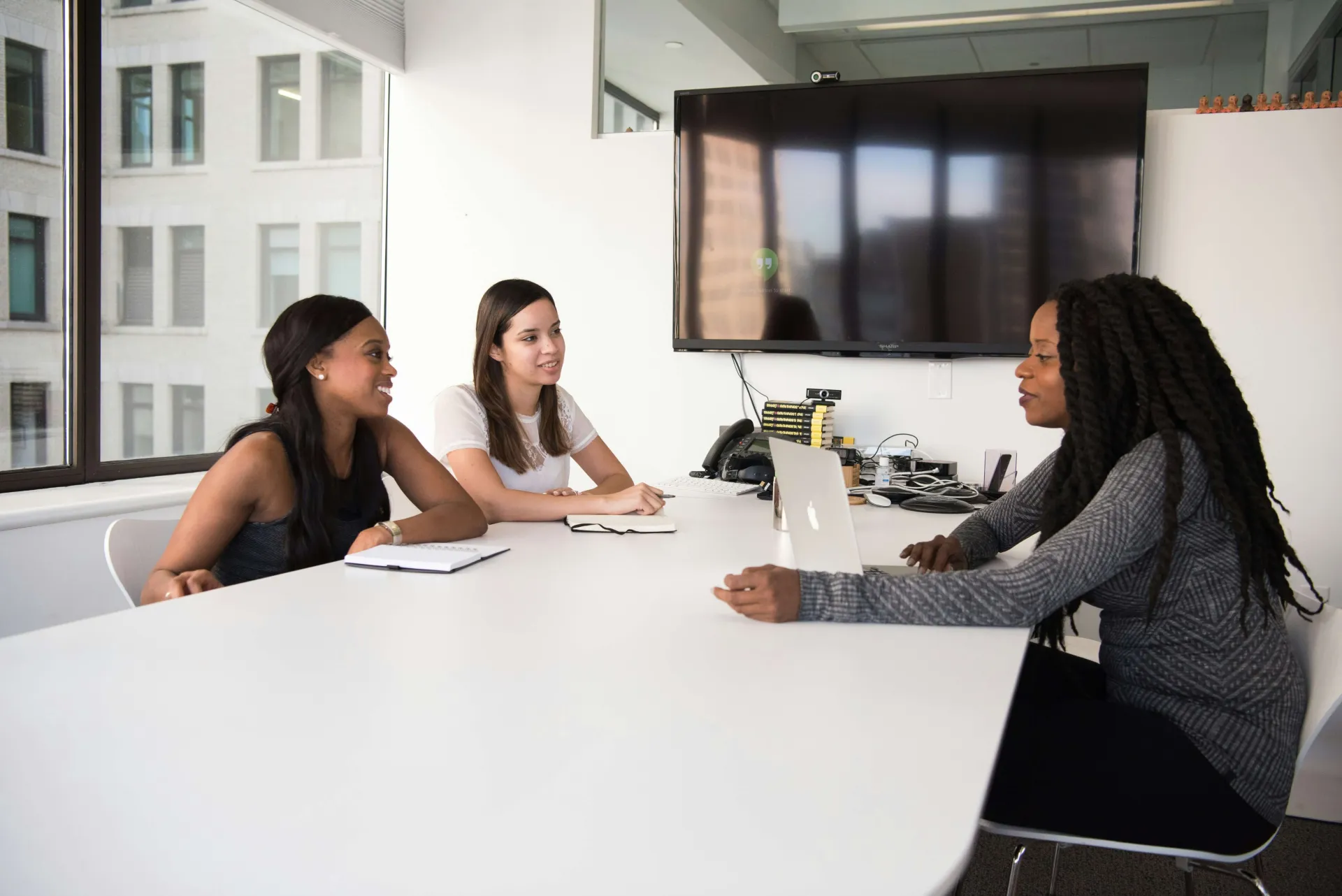 Three people are sitting at a white conference table, talking in an office setting.