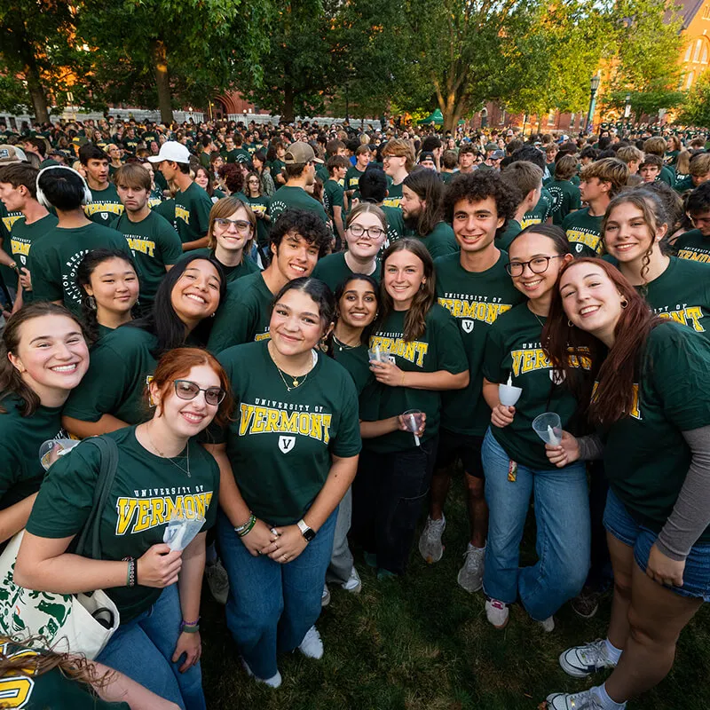 Group of students in green University of Vermont t-shirts holding candles grouped together on the university green.