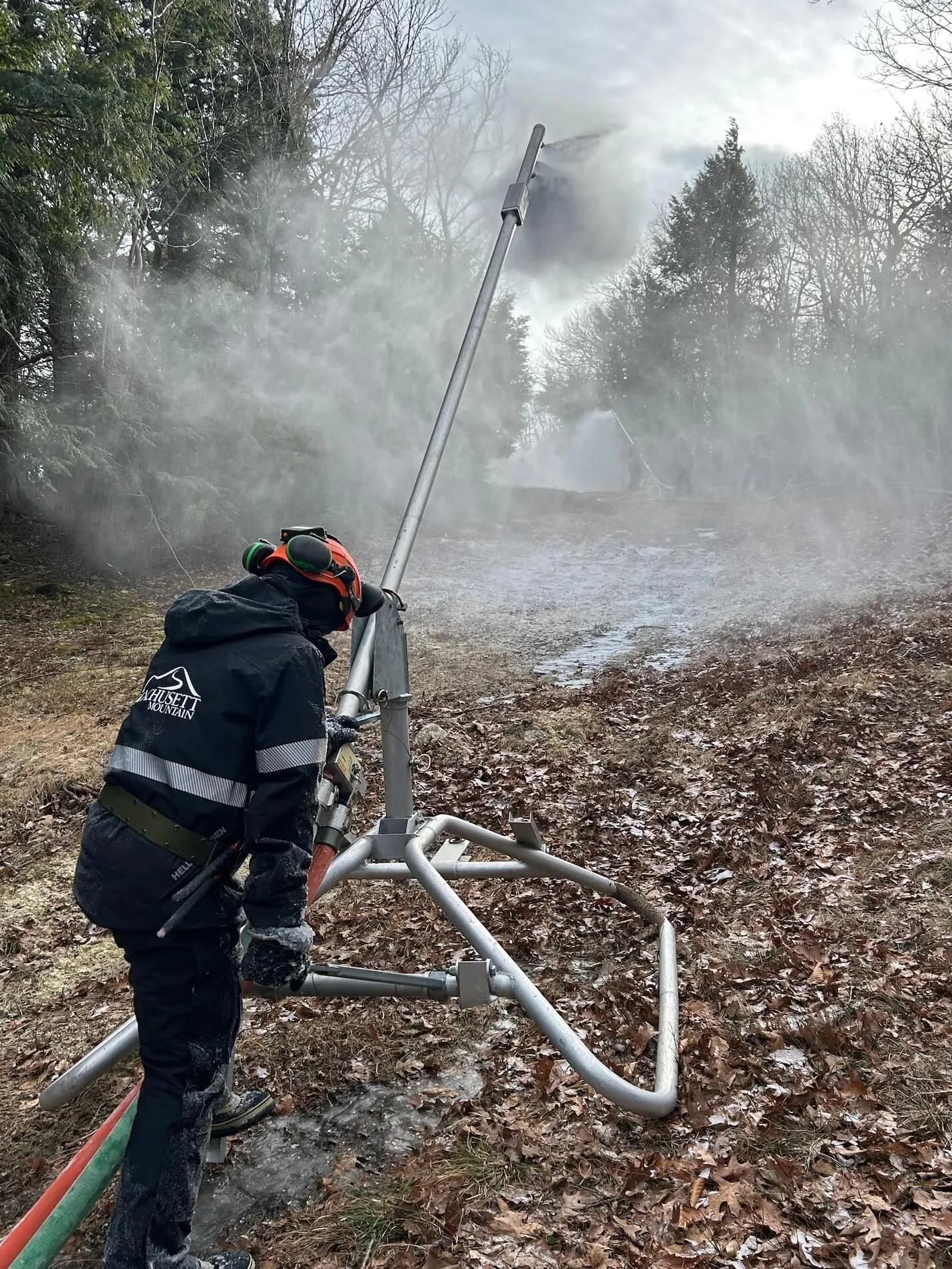 A person in a coat and helmet operating a snowmaking machine.