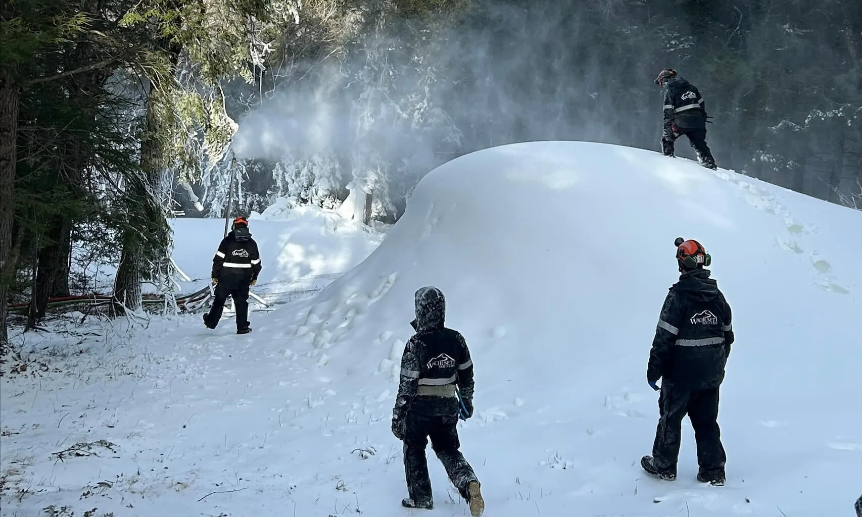 A group of people on a ski mountain watching a snowmaking machine.