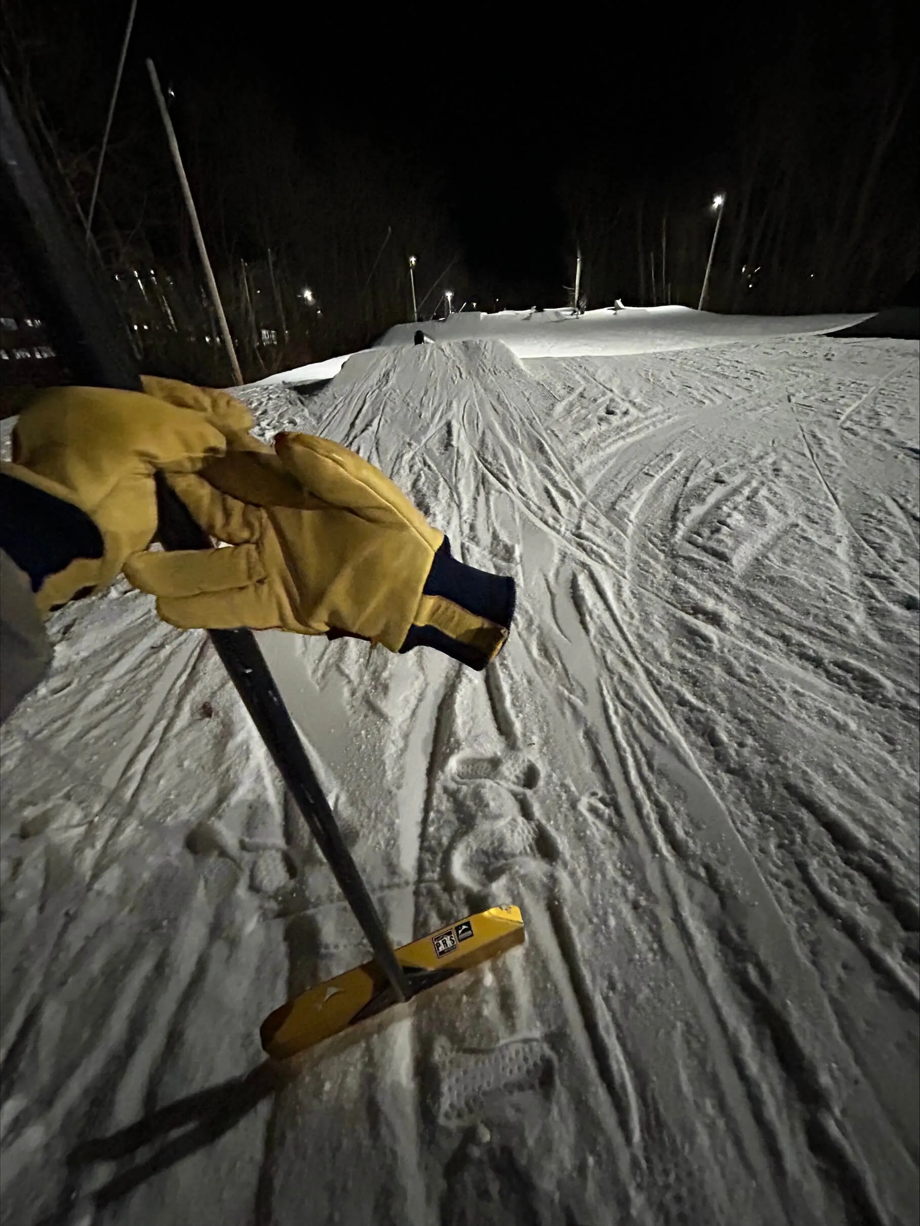 Leo holding up snow grooming equipment on a mountain at night.