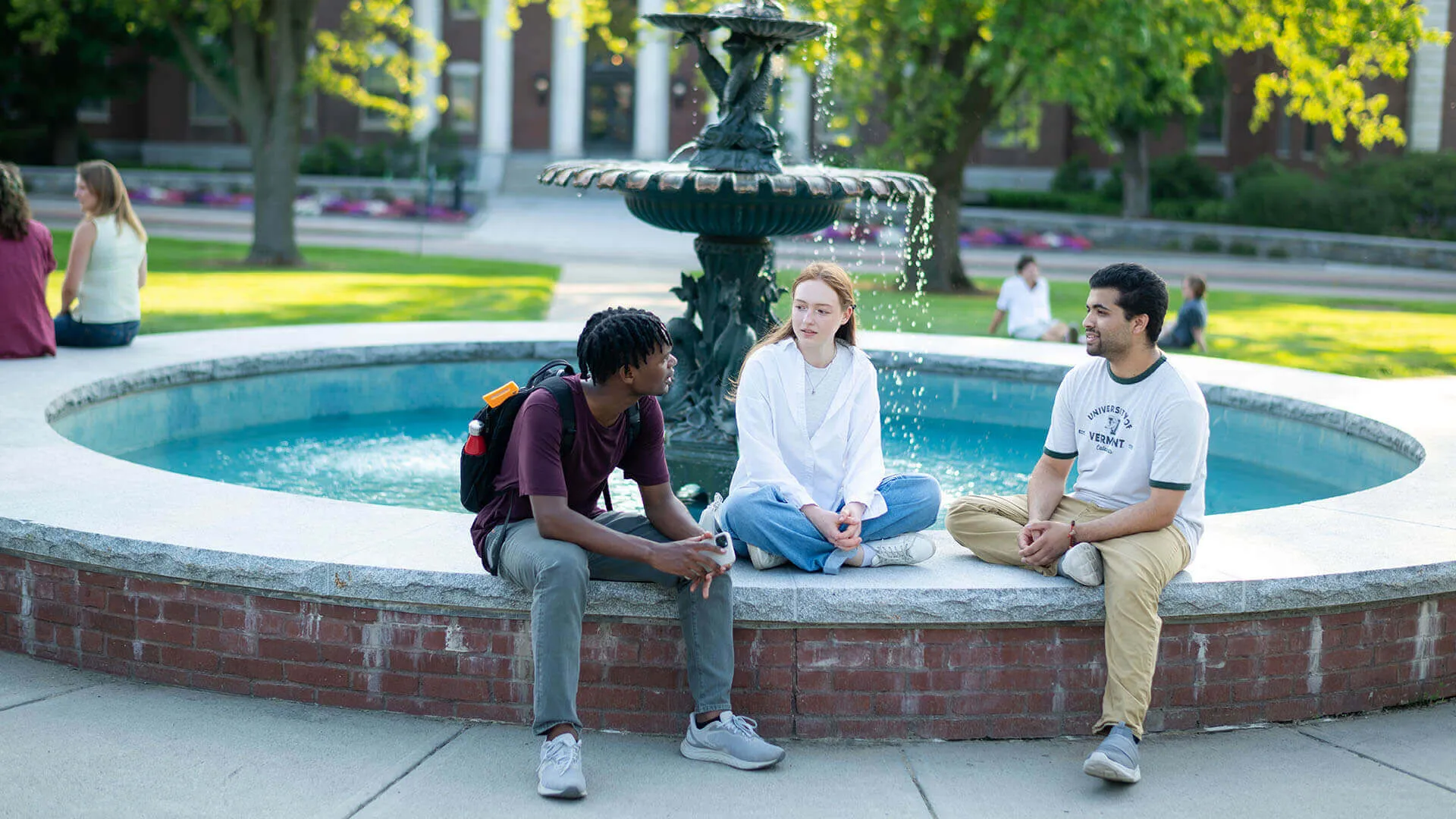 Students sitting and talking by a campus fountain on a sunny day.