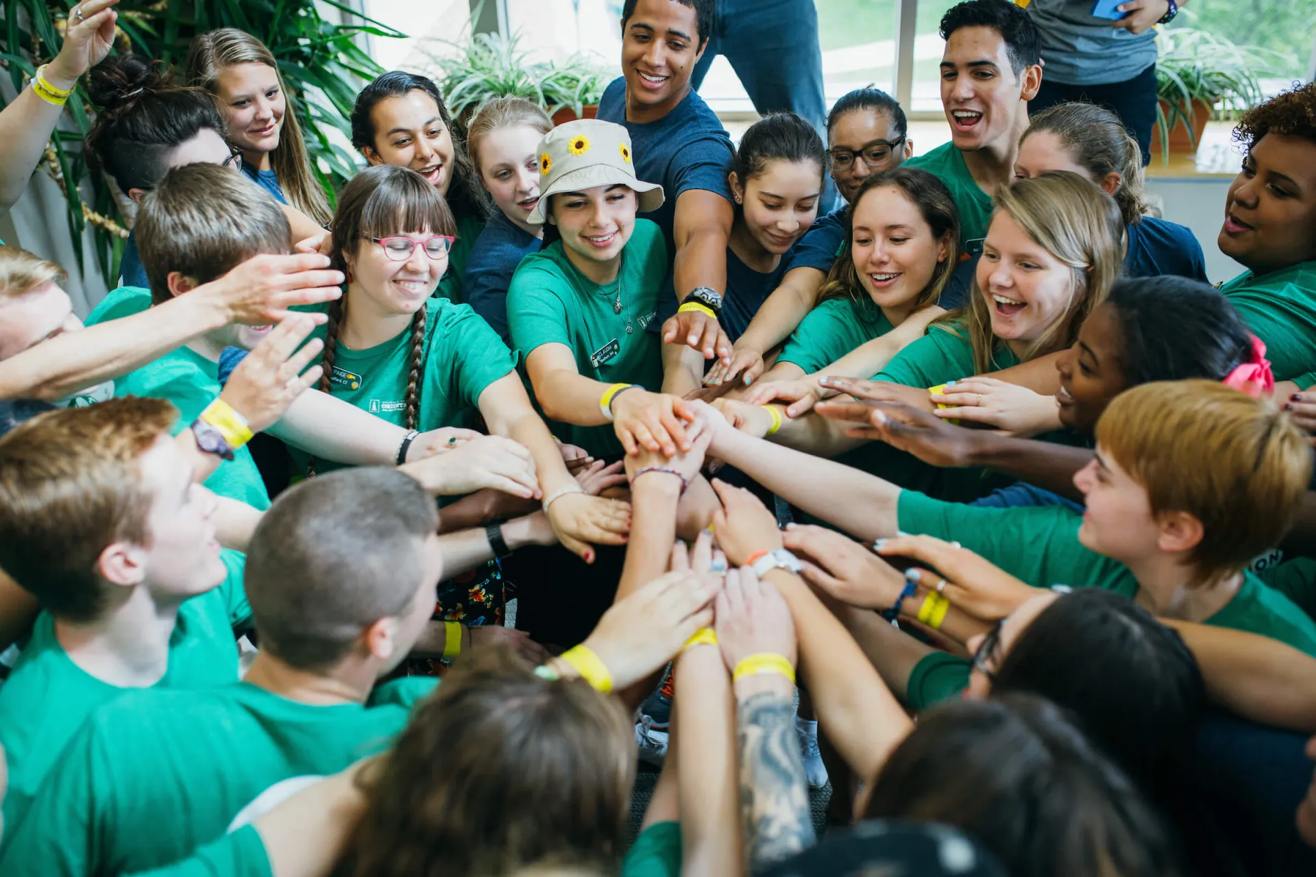 A large group of students smiling and joining hands in a team huddle.