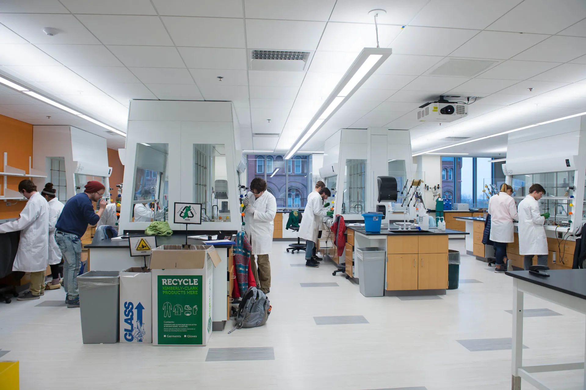 Students working in a bright, chemistry lab with fume hoods and lab benches.