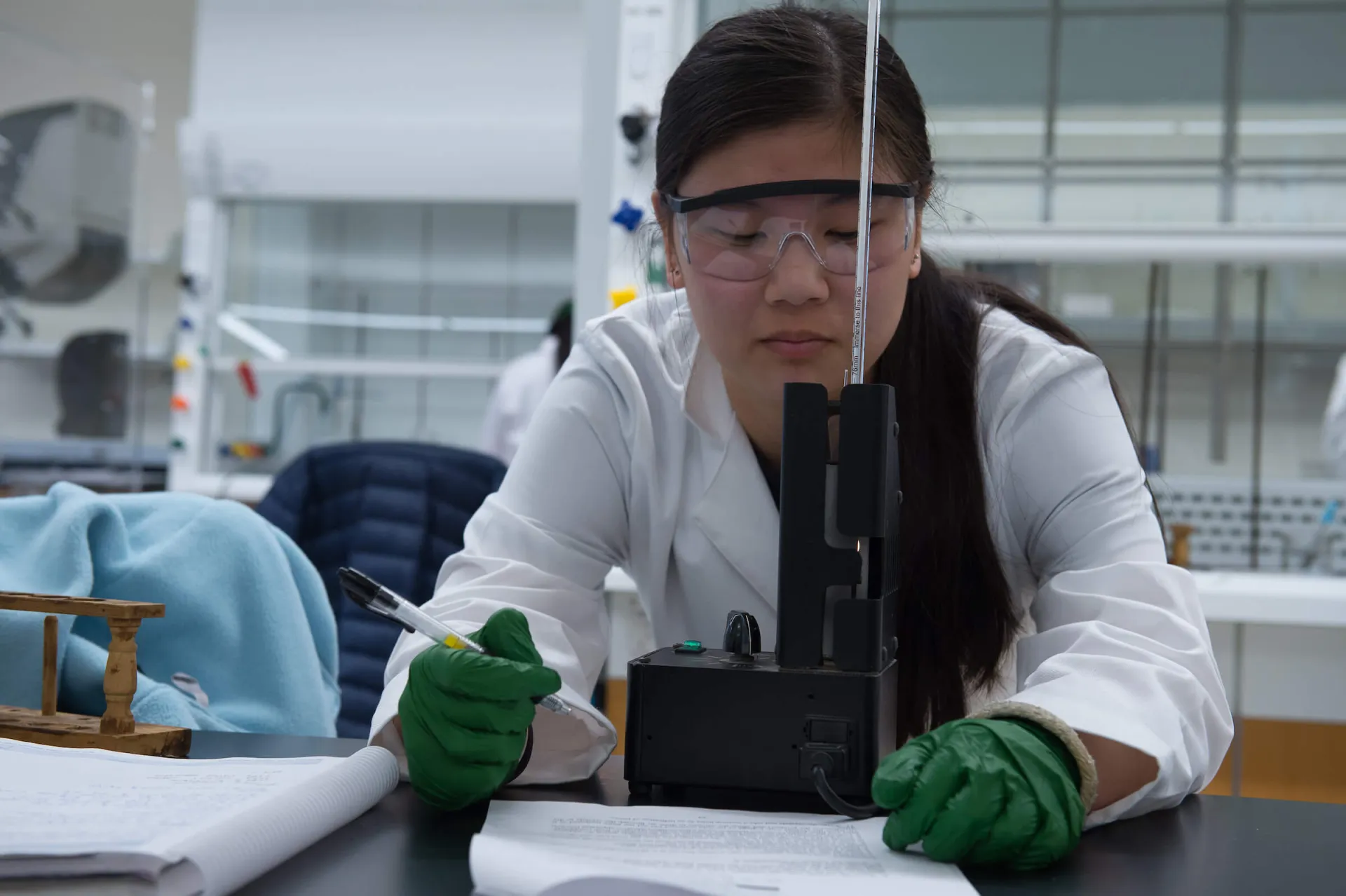 Student in a chemistry lab measuring a sample while wearing safety goggles and gloves.