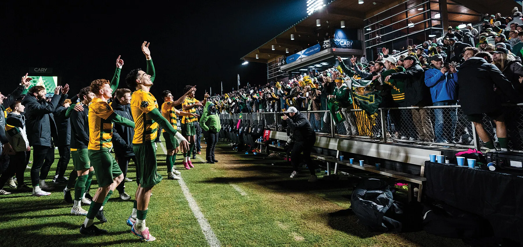 soccer players on a field cheer with fans in the stands