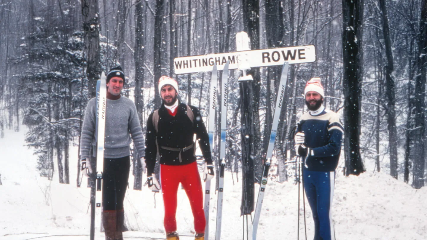 three men wearing winter clothes stand in the snow in front of a sign that says whitingham rowe