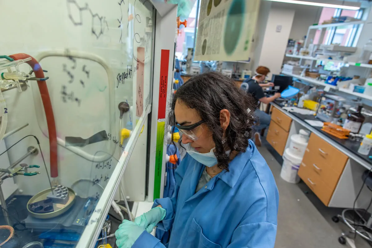 Researcher working at a fume hood in a chemistry lab while wearing safety gear.