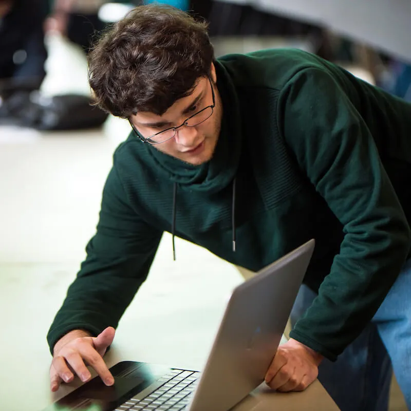 Person leaning over a laptop and typing while focusing on the screen.