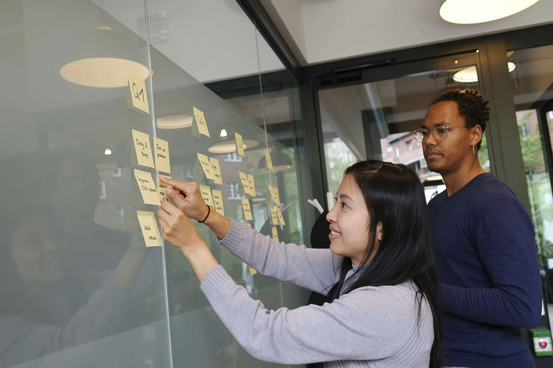 Two people brainstorming together, placing sticky notes with ideas on a glass wall in a modern office.