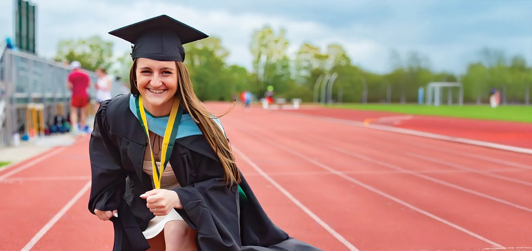a student in a graduation cap and gown poses on a track