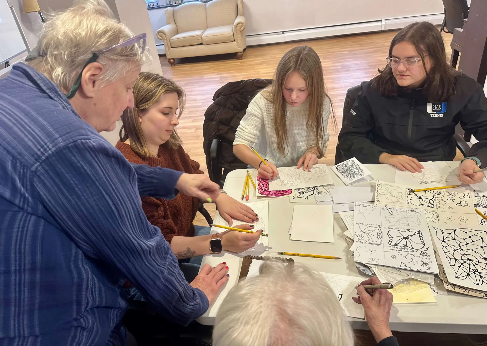 Students and older adults drawing at a table during an art workshop