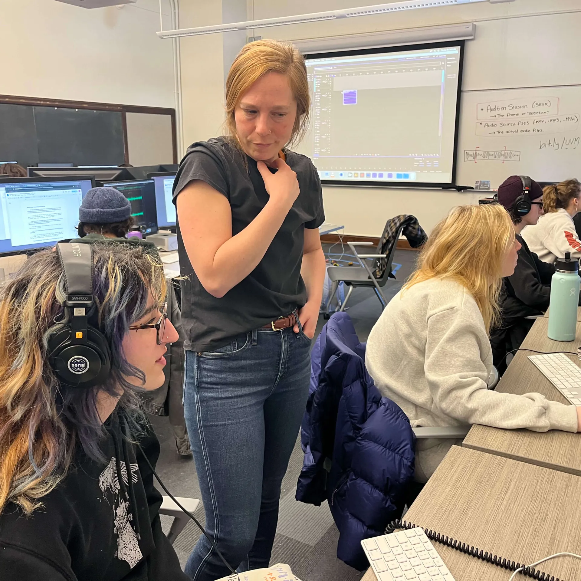 A person assists students working on audio projects in a computer lab.
