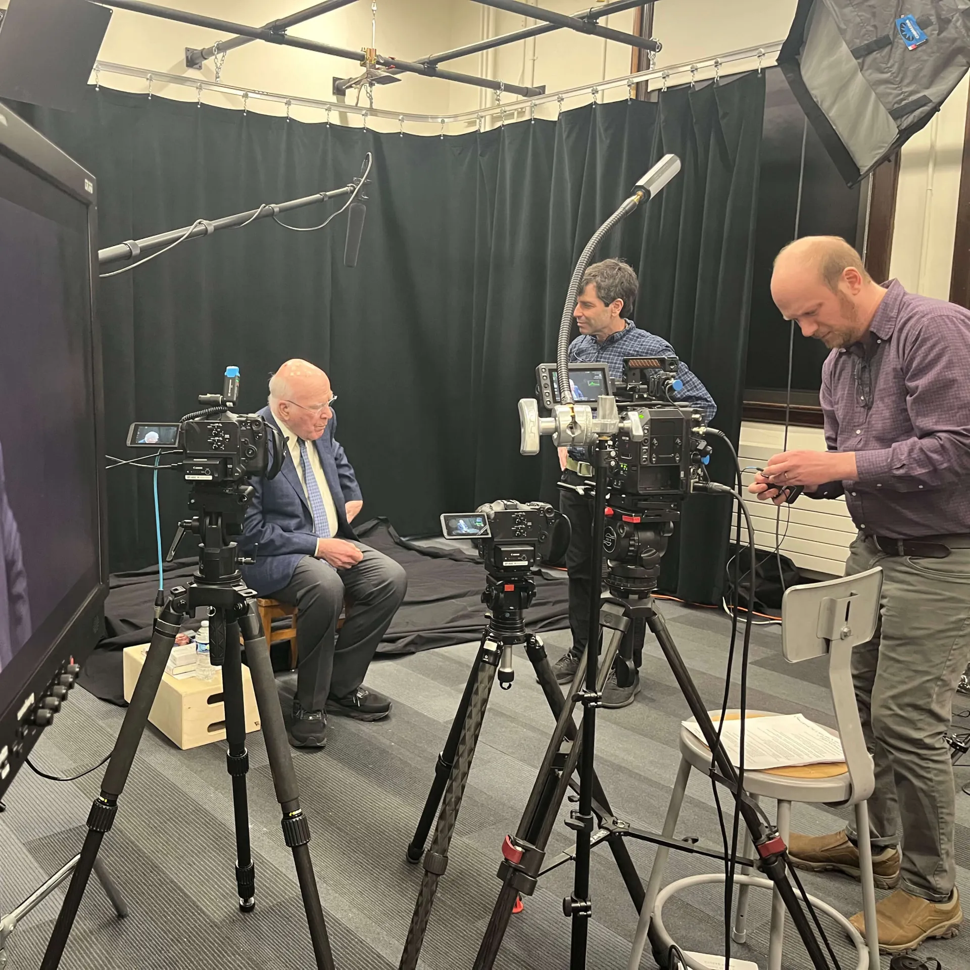 A crew films an interview in a studio with cameras and lighting equipment.
