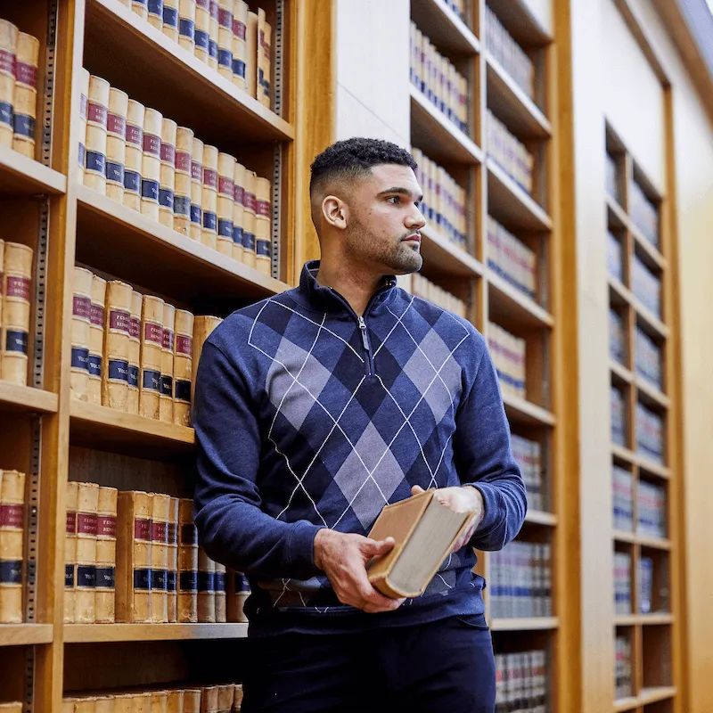 Person holding a book while standing between tall shelves of law books in a library.