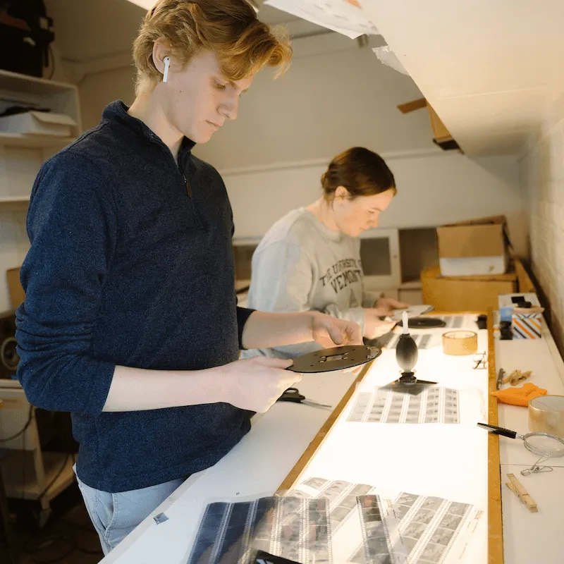 Two people working at a light table, examining and preparing film negatives in a photography workspace.