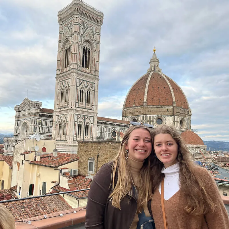 Two students stand in front of Florence Cathedral, with the cathedral’s dome and bell tower visible behind them in Florence, Italy.