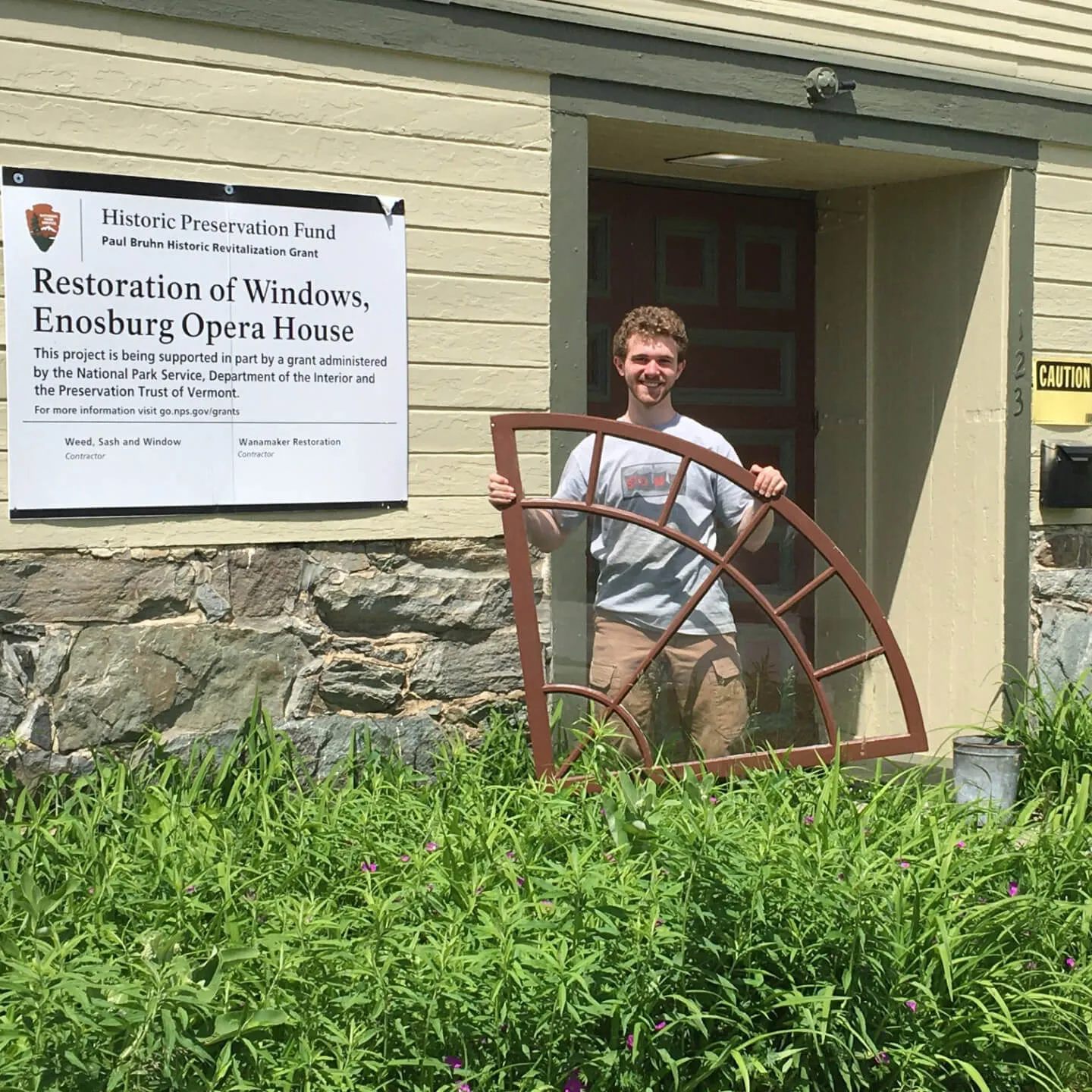 Person holding an arched window frame outside a historic building.