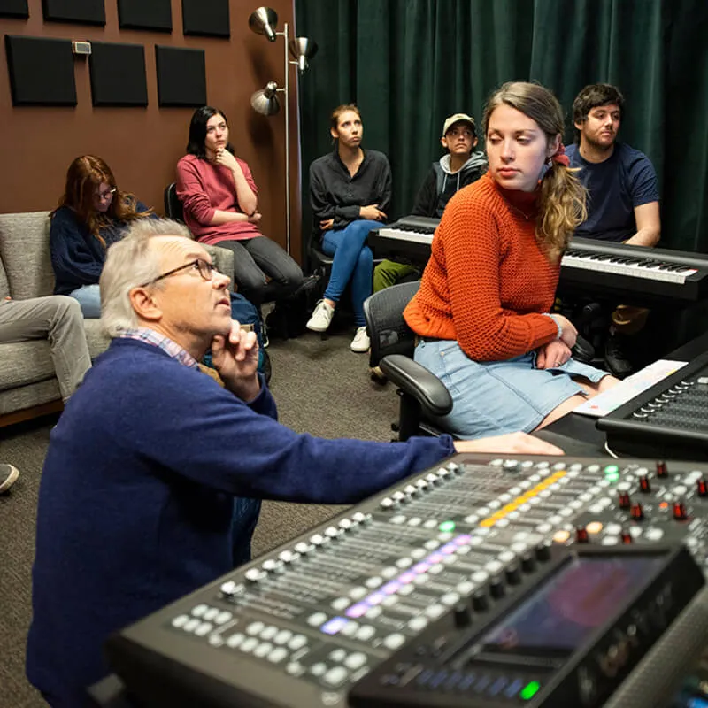 Students observe an instructor working at a sound mixing console in a recording studio.