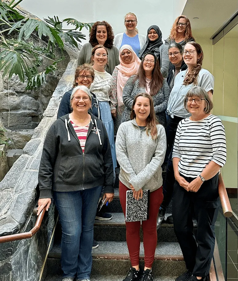 Group of individuals posing on a set of stairs with a stone railing and wall