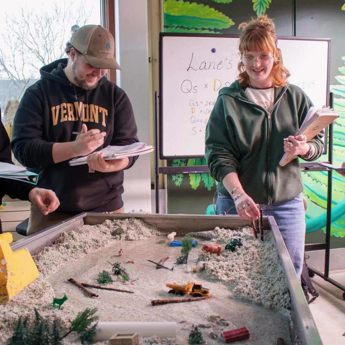A group of students interacting with an indoor representation of a river experiencing a flood event