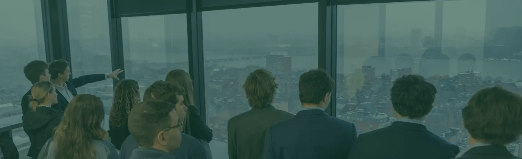 Students in business attire stare out office building windows at the city below.
