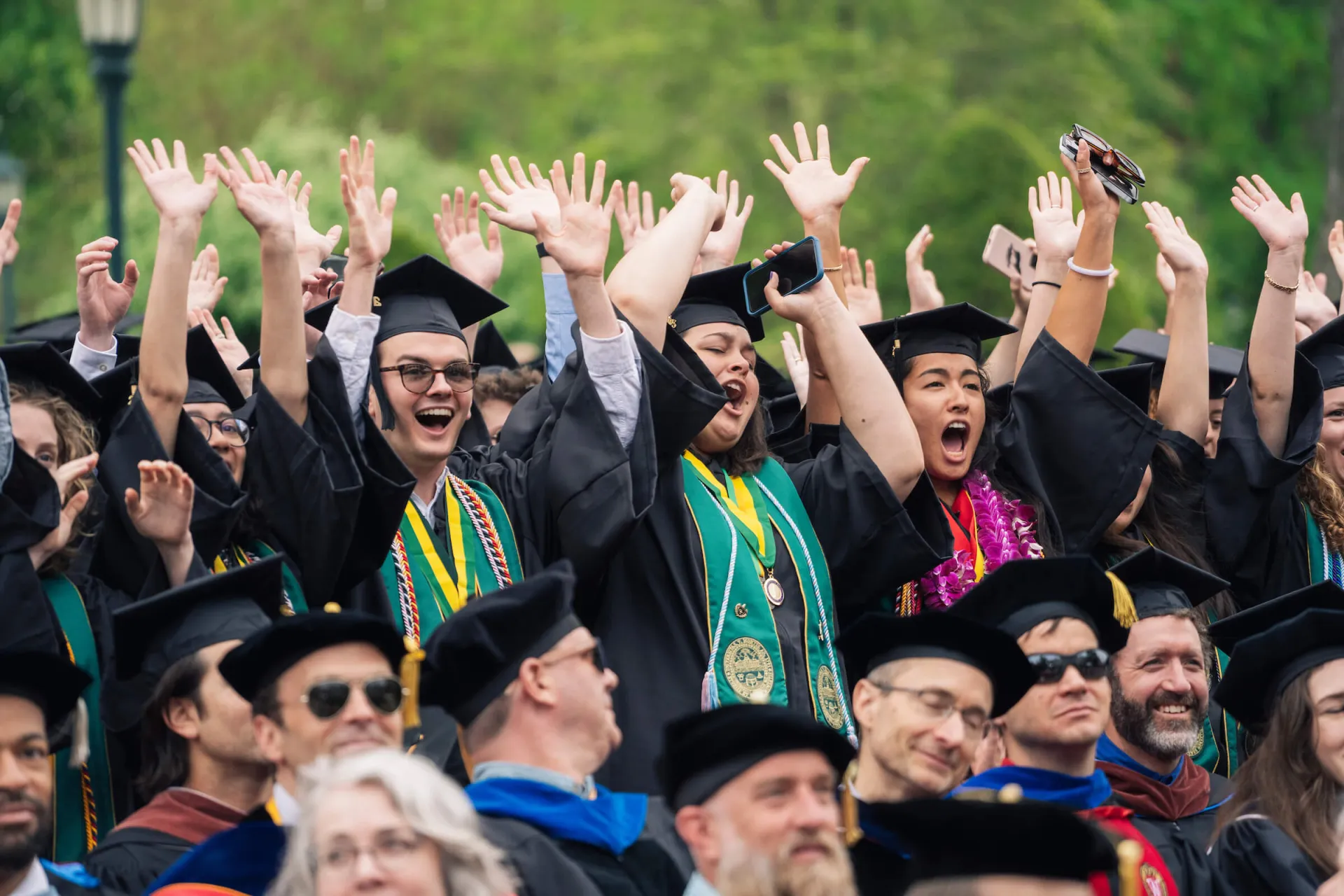 Celebrating graduates lift their hands into the air.
