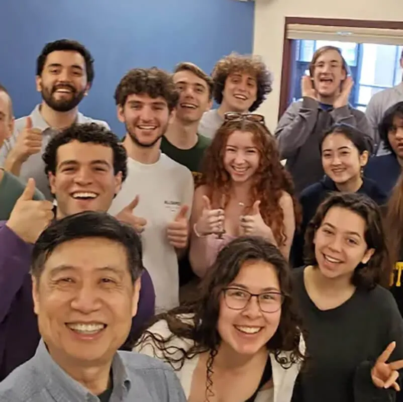 Chinese faculty member taking a smiling group selfie with students in a classroom.