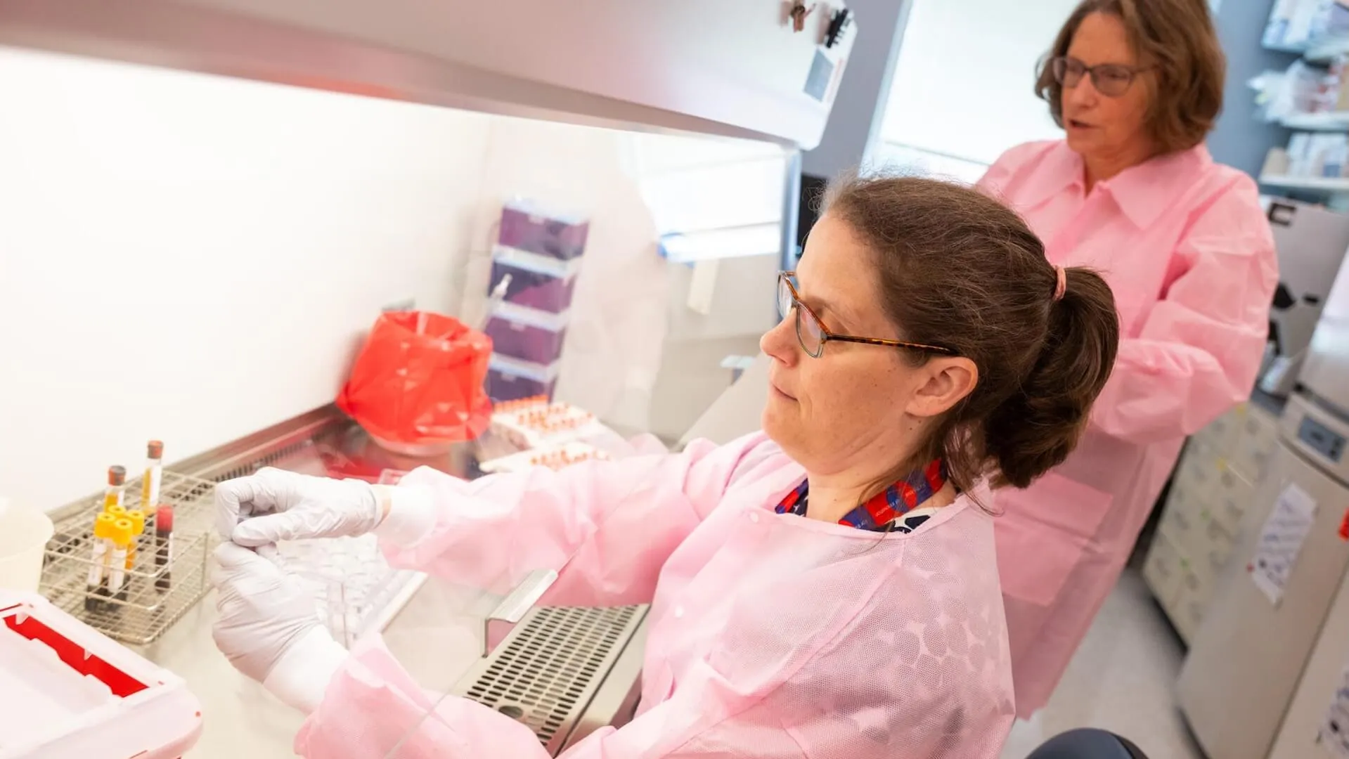 A scientist work at a lab bench while another looks on