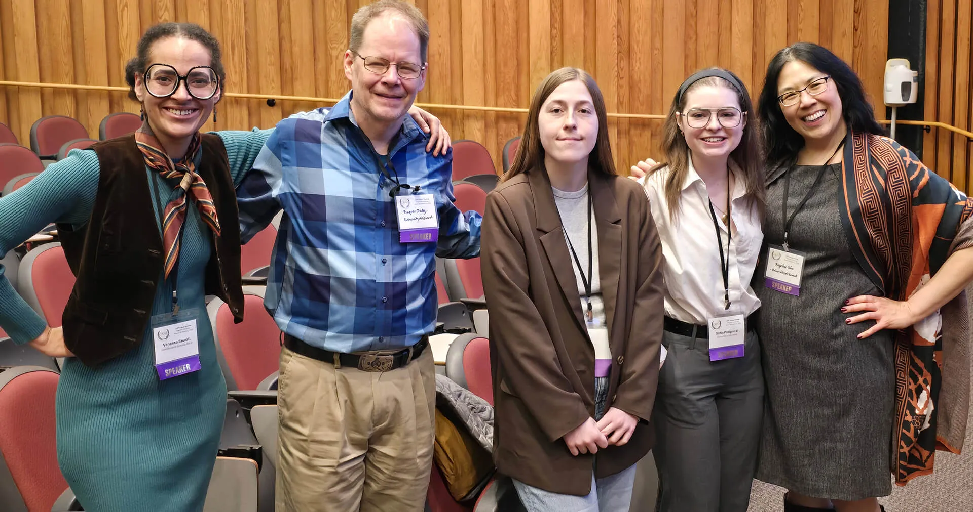 Five people standing together and smiling in a lecture hall.