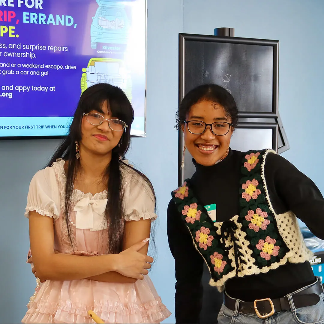 Two young adults smiling indoors, posing together in front of a screen.