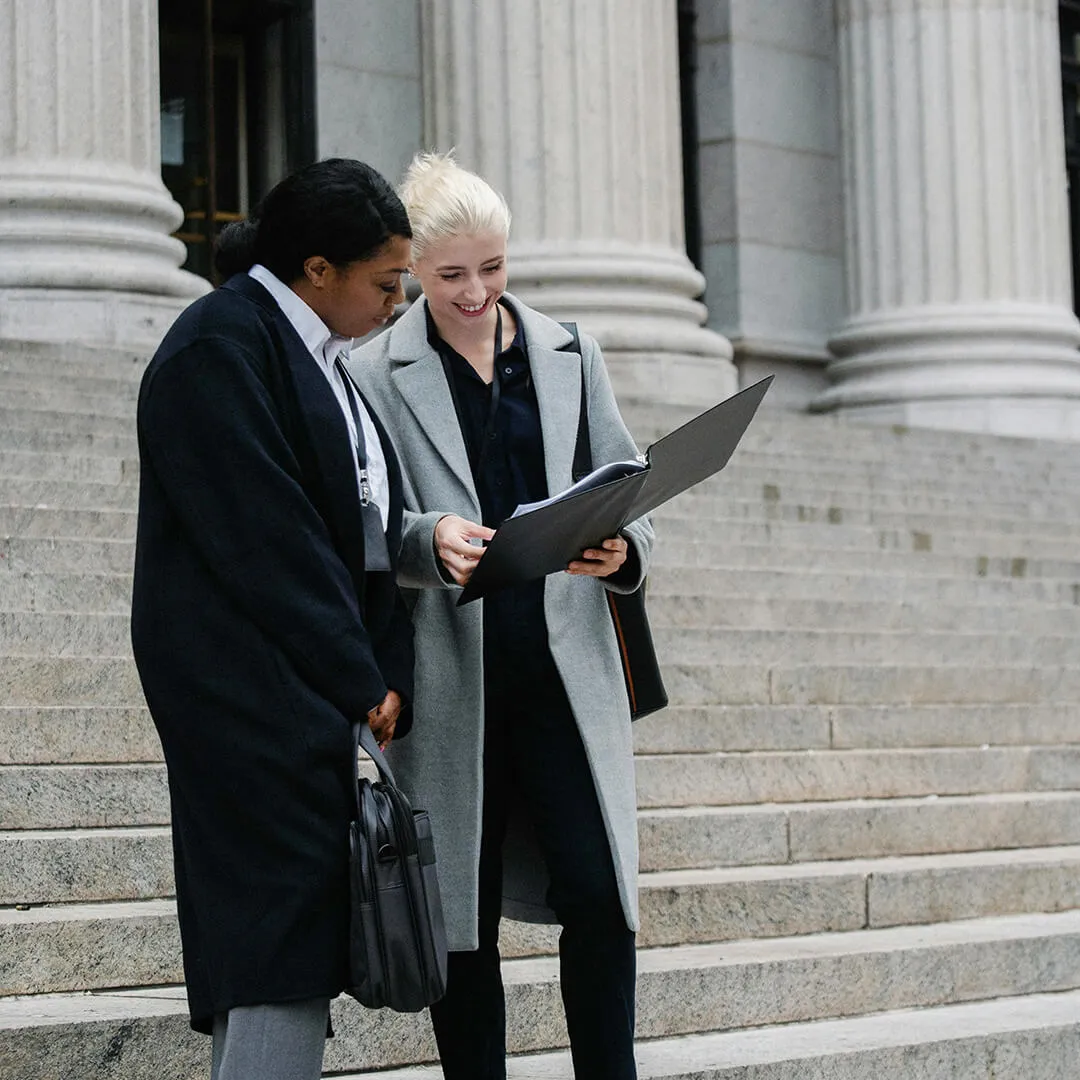 Two professionals standing outside a courthouse, reviewing documents together on the steps.
