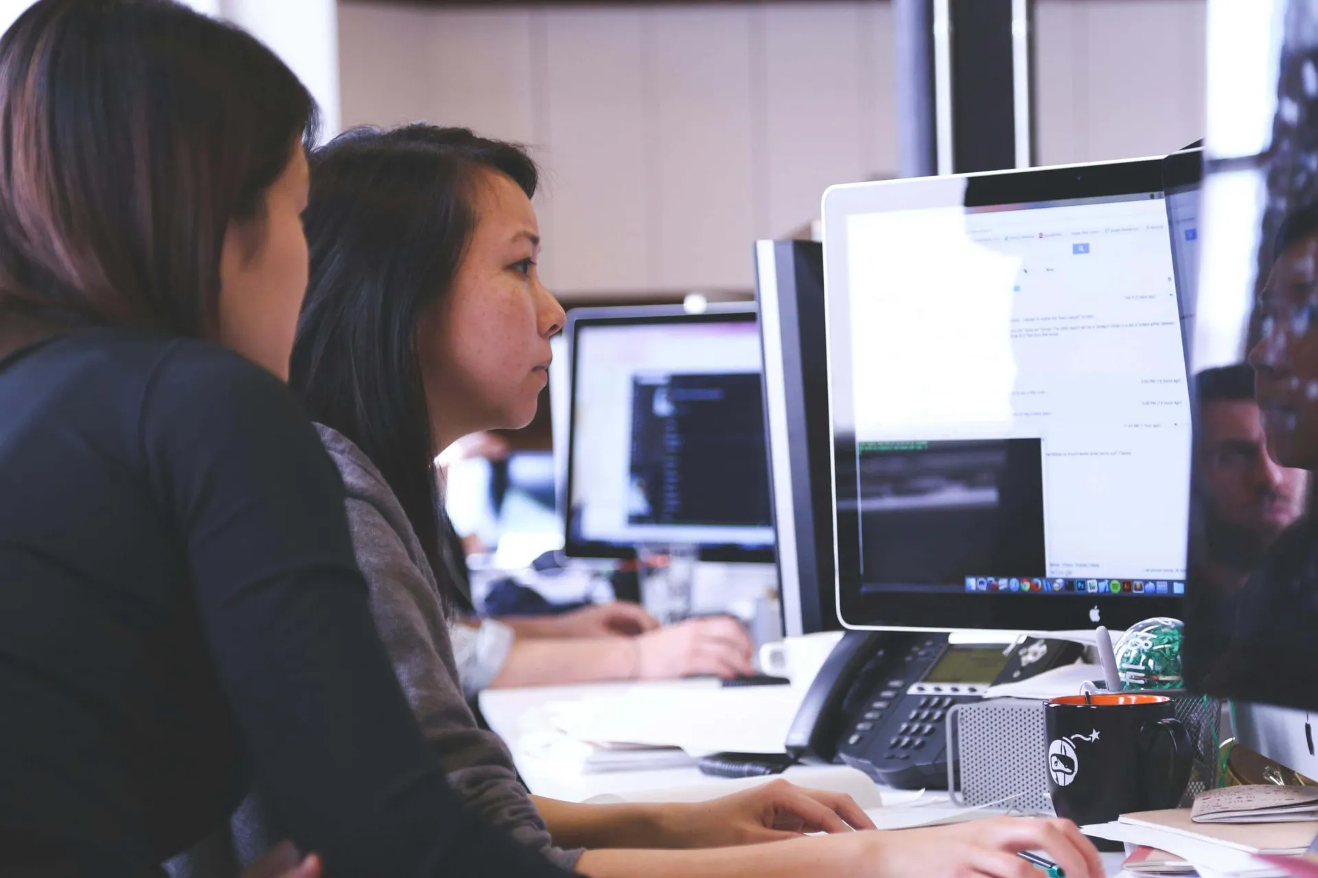 Two women peer intently at a flatscreen monitor in an office