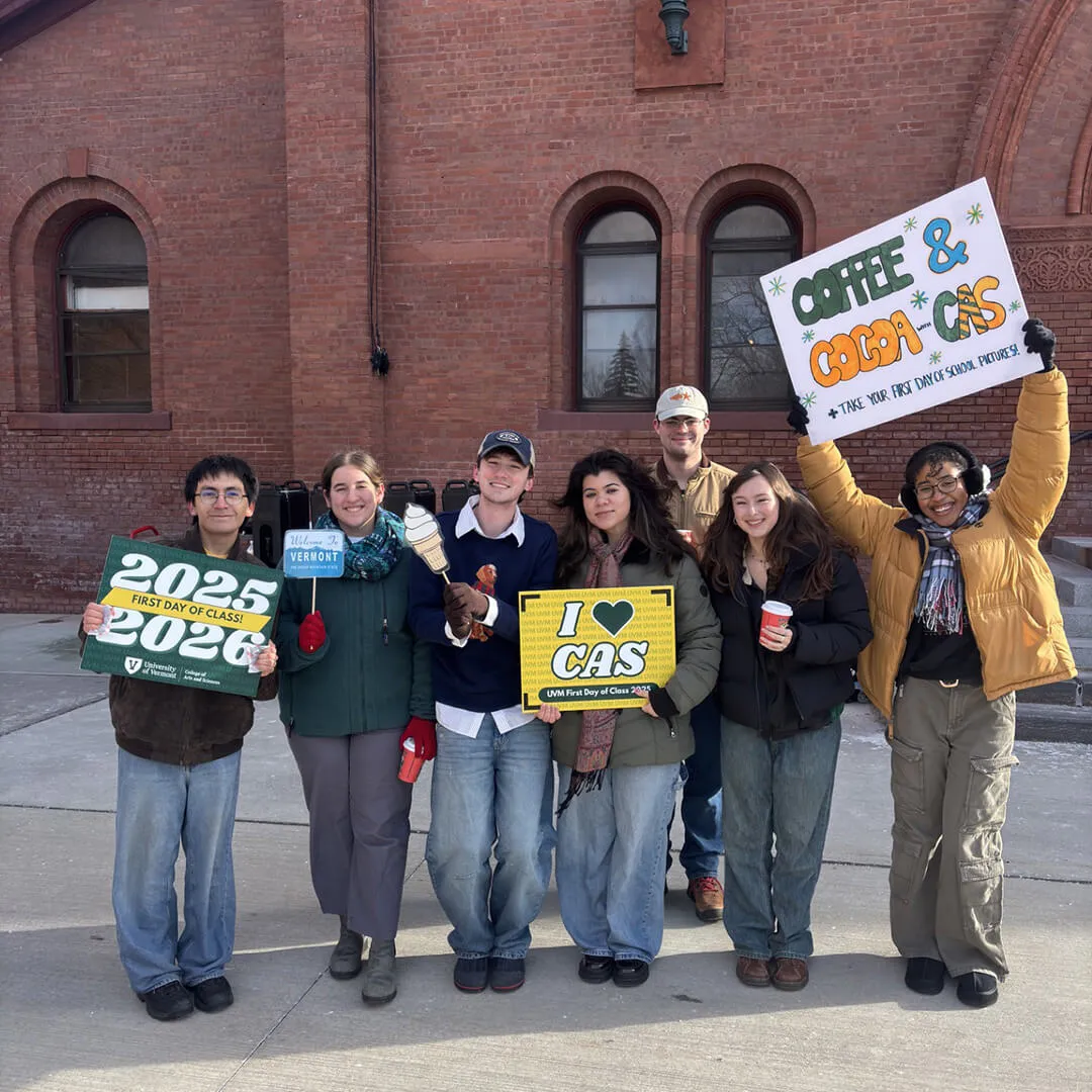 Group of students posing outside a brick building, smiling and holding event signs.