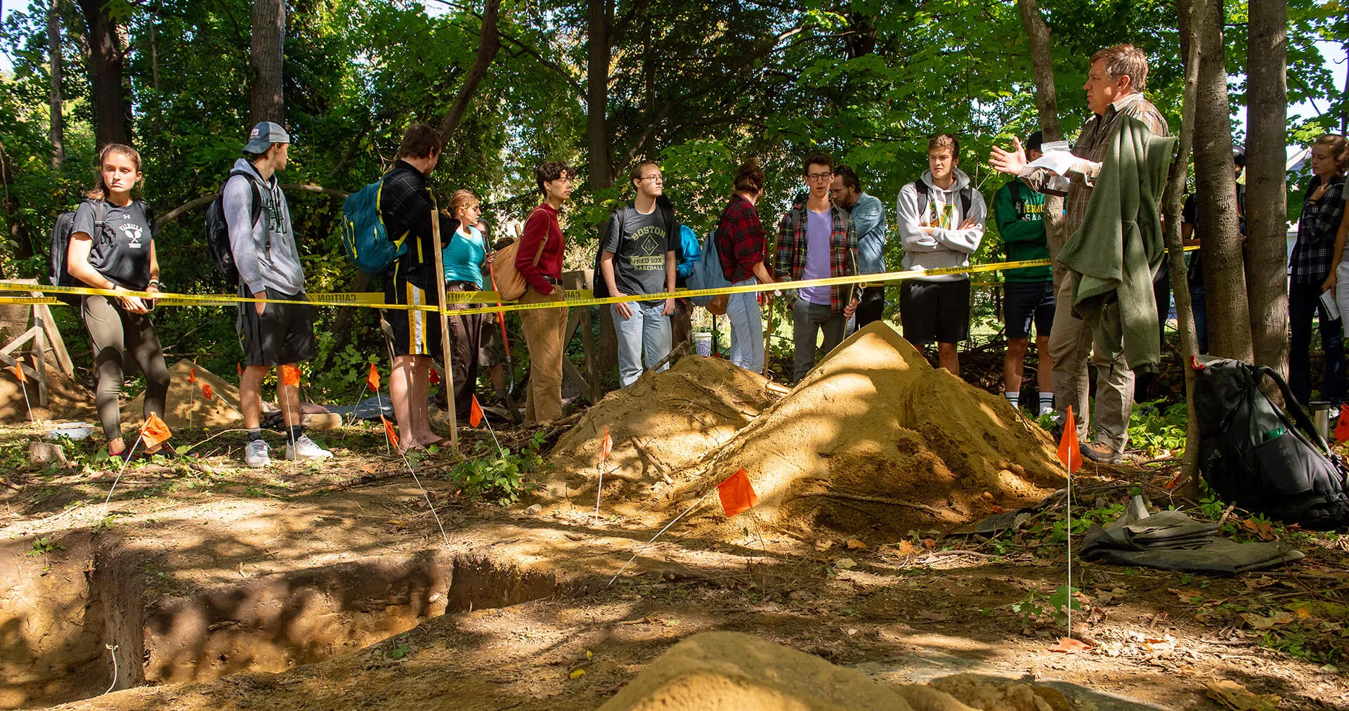 Students listening to an instructor at an archaeological excavation site during a fieldwork course.
