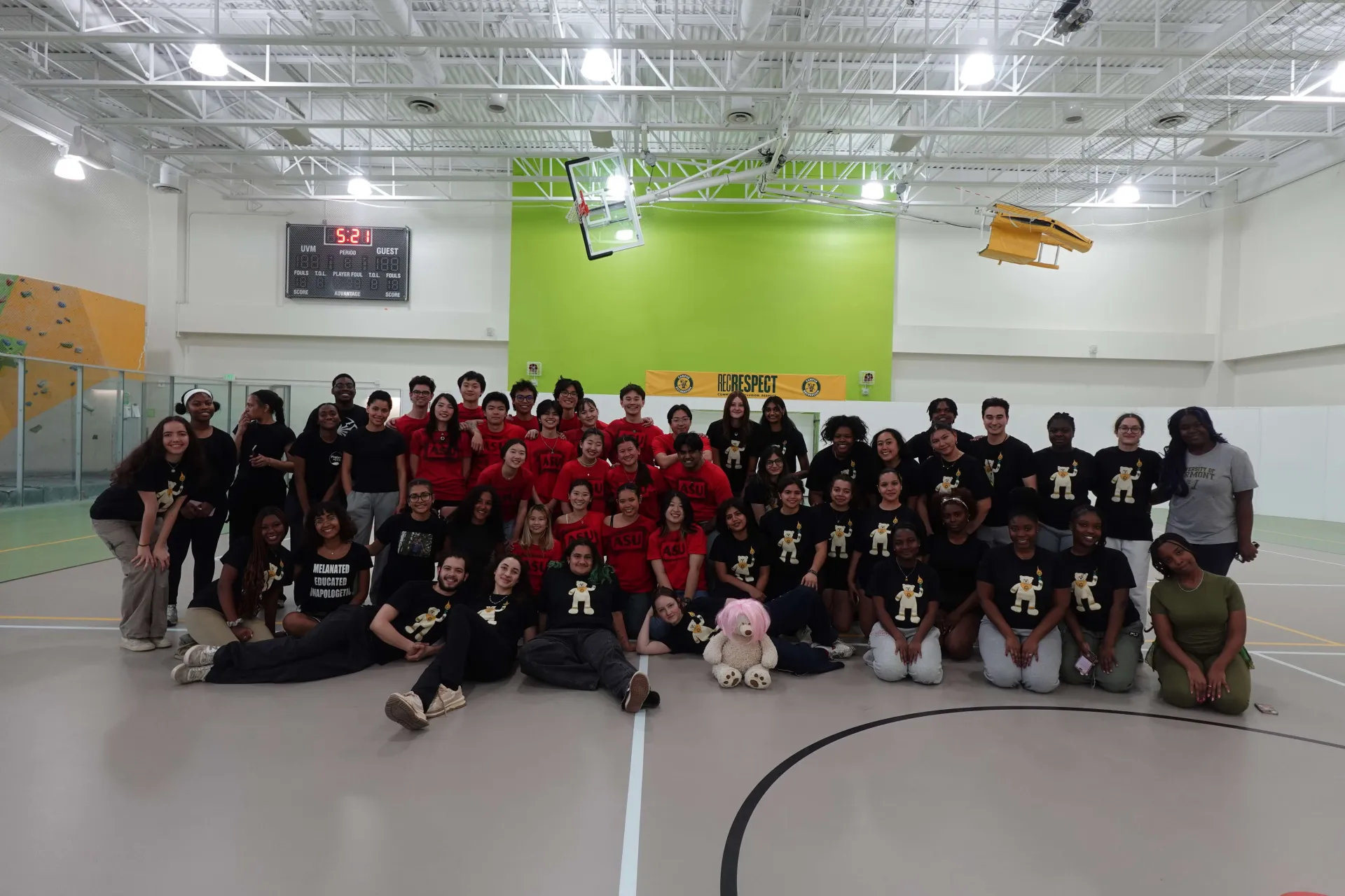 A large group of students all in Mosaic Olympic t-shirts sitting on the campus recreational floor 