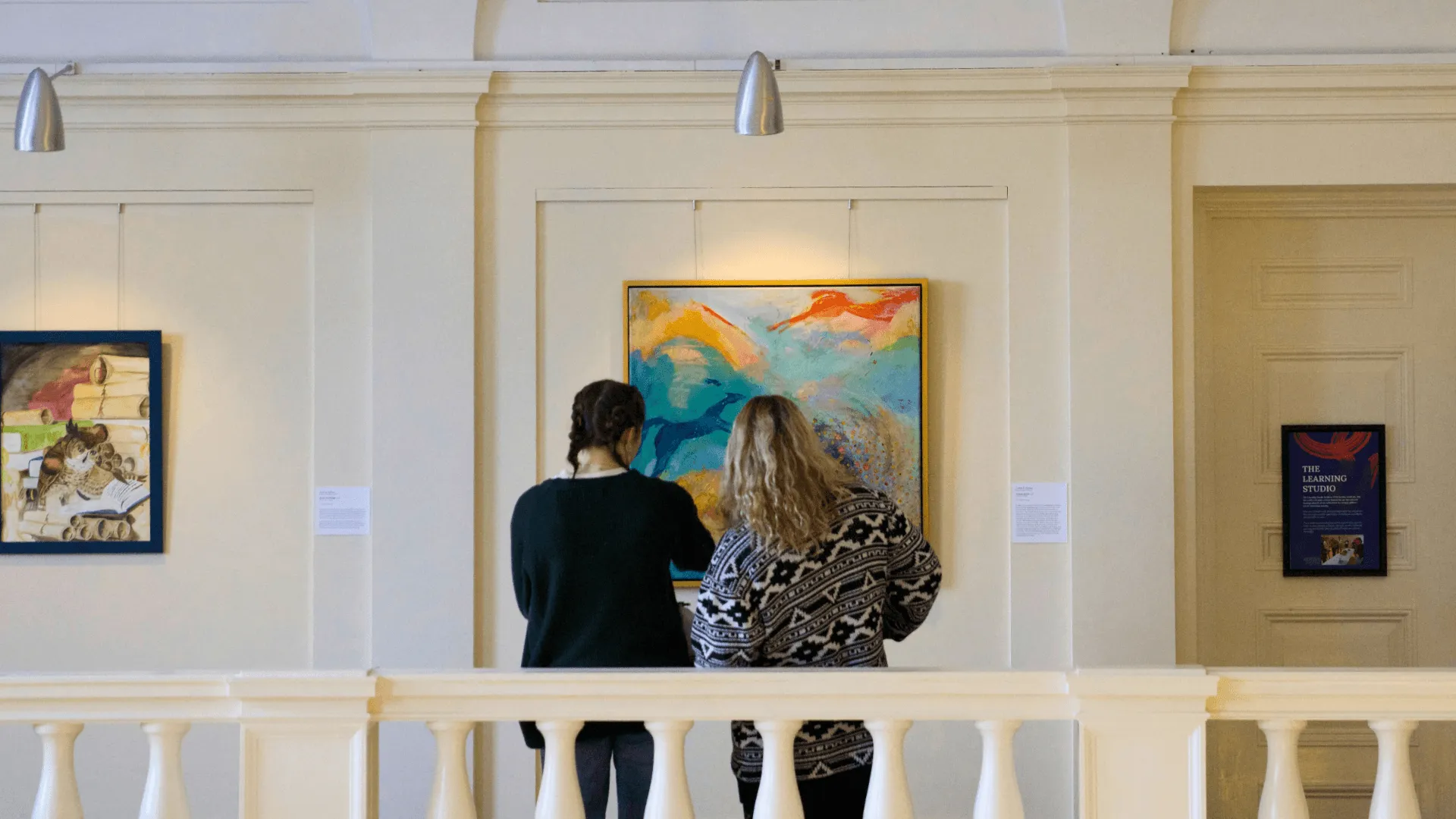Two visitors look closely at a painting.