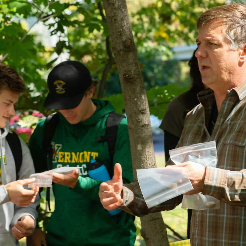 Professor distributes sample bags to students outdoors.