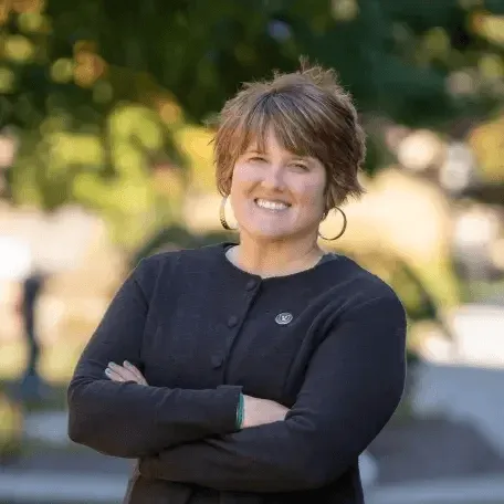 Kellie Campbell portrait. Woman with short hair, black sweater, arms crossed, smiling at the camers