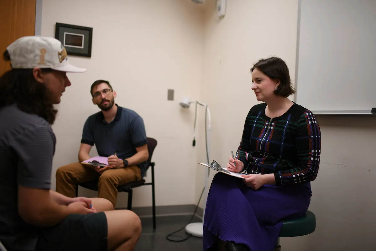 student sitting and taking a history from a patient with a teacher sitting and looking on.