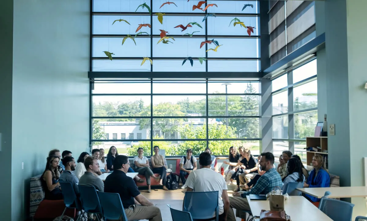 Students sitting in a circle in a room with large high windows