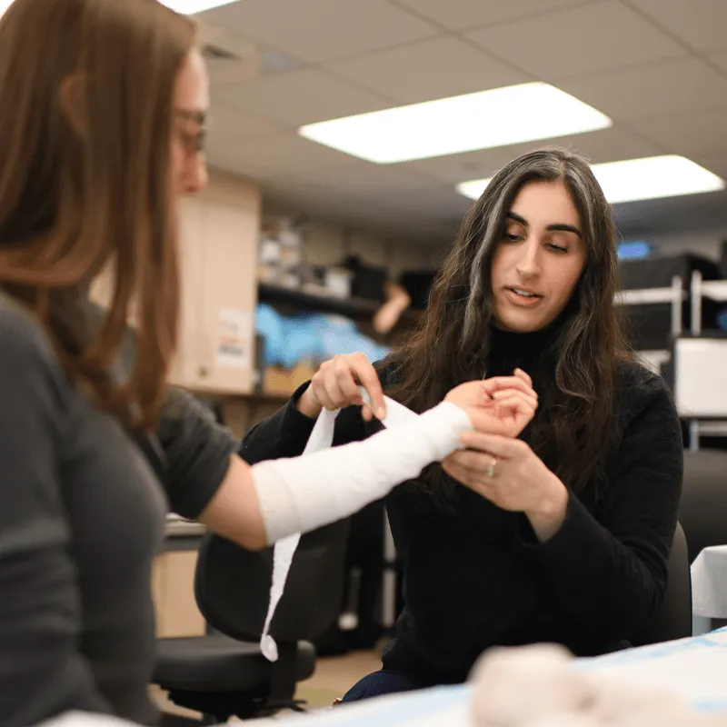 Person wrapping another person's arm in gauze. 